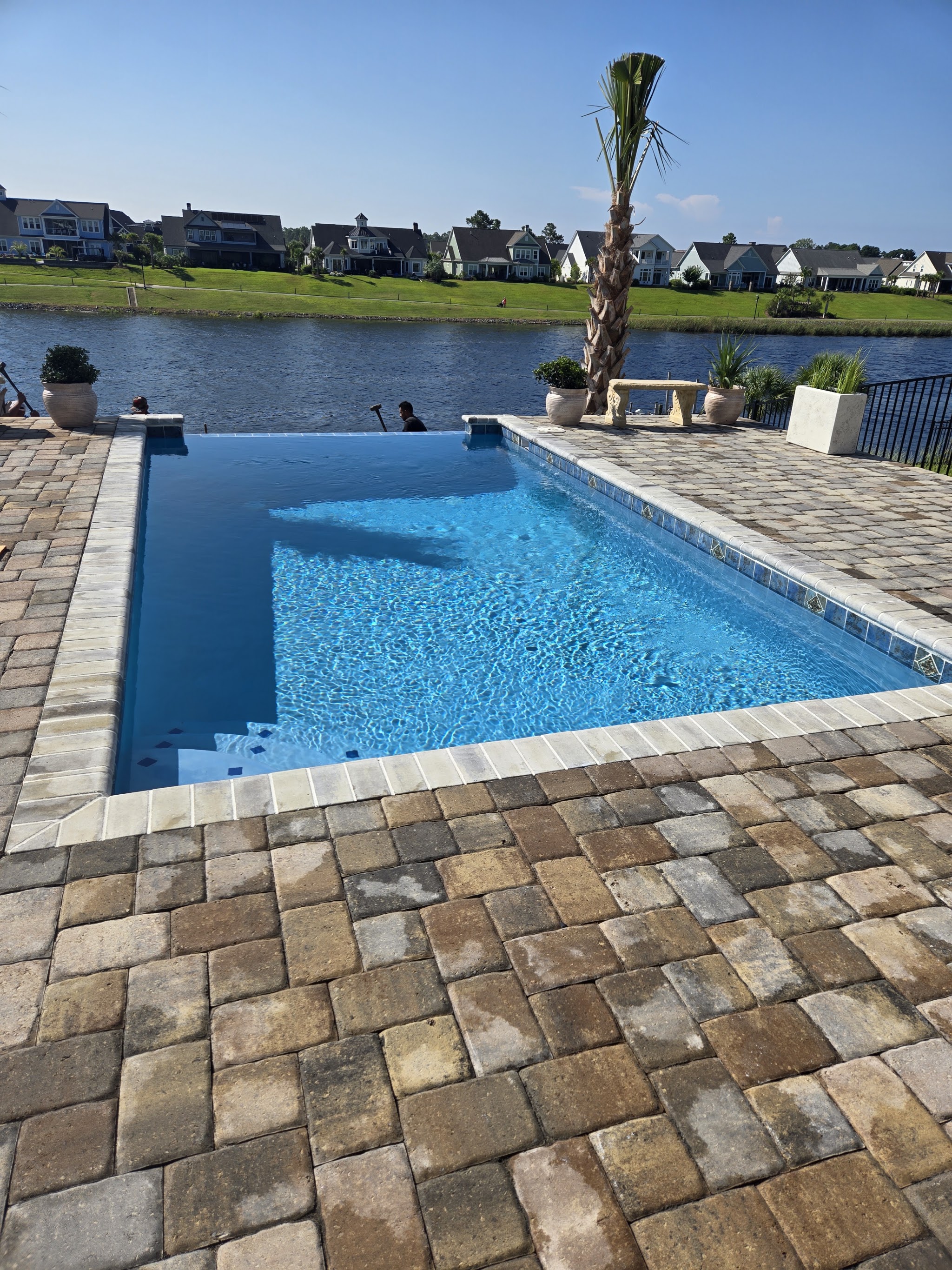 Lap pool with a paver deck beside a pond